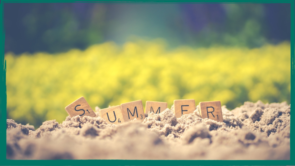 The word summer spelled out on scrabble tiles placed in sand.